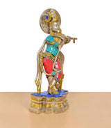 Three-quarter side view of Krishna flute idol; brass figure with teal sash and red accents