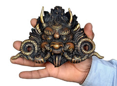 Brass cheepu mask in front view held in hand, ornate dragon face