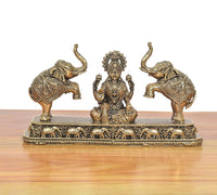 Seated Lakshmi idol with crown and jewelry, flanked by two elephants on detailed base.