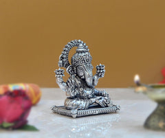 Seated Vinayak Ganesha statue in brass-tone, ornate base and raised hands.