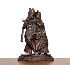 Brass Radha Krishna idol, front view with raised arms, crowns, and layered jewelry details.