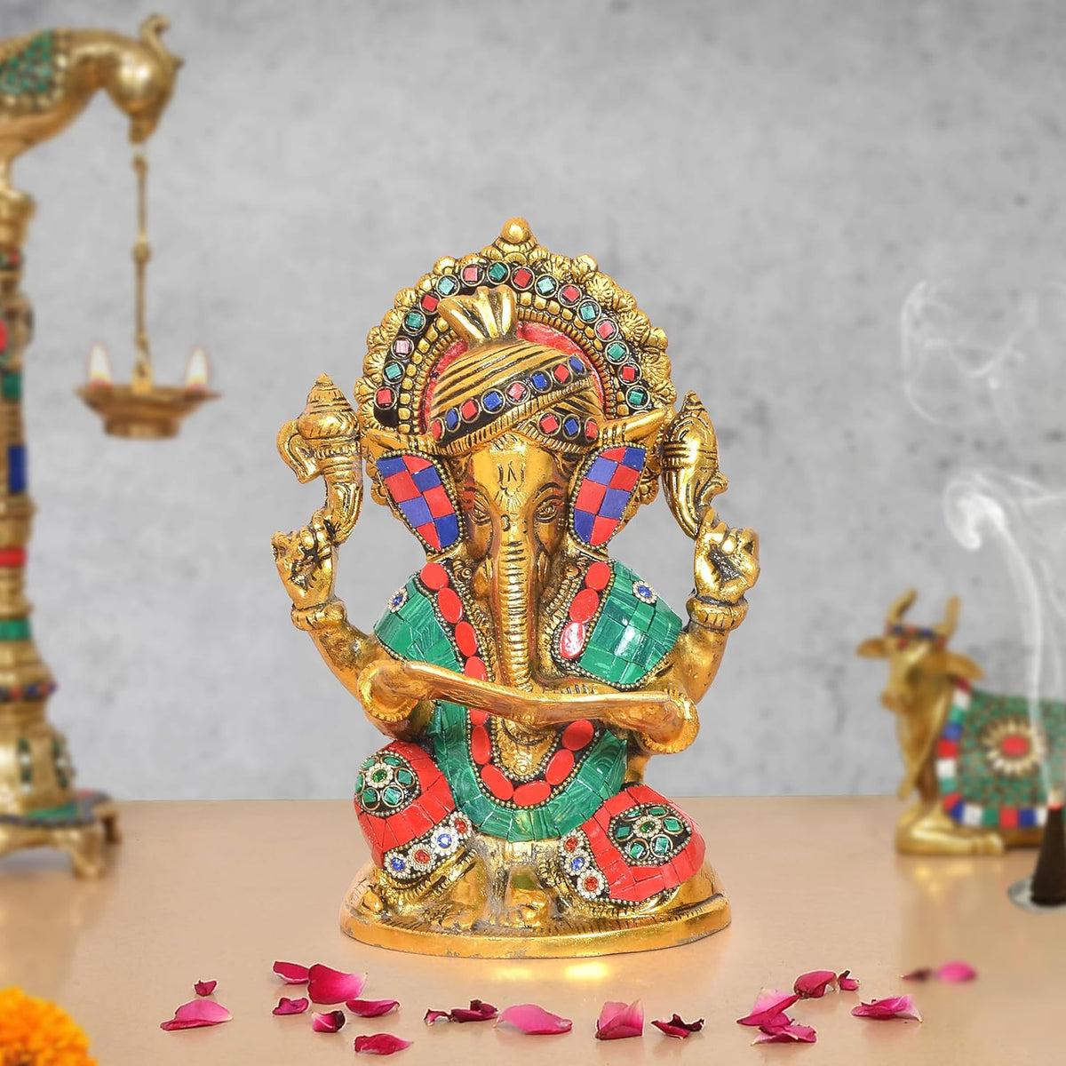 Gold-tone metal Ganesha idol with jeweled crown and colorful outfit, holding a scroll