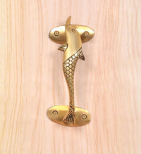 Close-up golden brass dolphin fish door handle with scale-textured body and screws