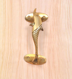 Close-up golden brass dolphin fish door handle with scale-textured body and screws