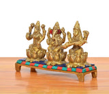 Angled view of golden brass Lakshmi, Ganesha & Saraswati idol set with painted base