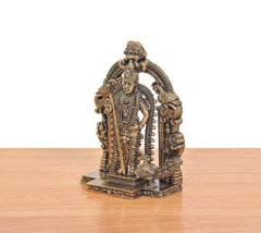 Brass Murugan statue side view, richly detailed garments and curved prabhavali arch