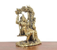 Brass Radha-Krishna idol on swing, side view showing seated pose and arch details.