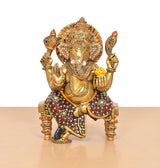 Ganesha statue in brass tone with colorful meenakari patterns, seated on chowki