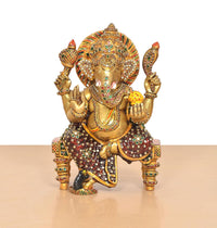 Ganesha statue in brass tone with colorful meenakari patterns, seated on chowki