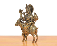 Brass MATA idol seated on goat, side view showing crown, instruments, and ornaments