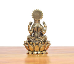 Back view bronze Lakshmi statue seated on lotus petals, textured garment and crown.