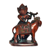 Rear three-quarter view of Krishna on cow idol, ornate patterned attire