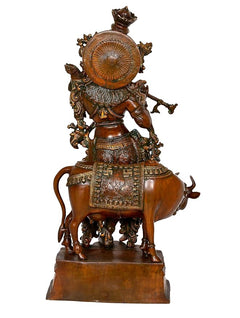 Krishna brass idol back view, large circular halo motif on cow figure