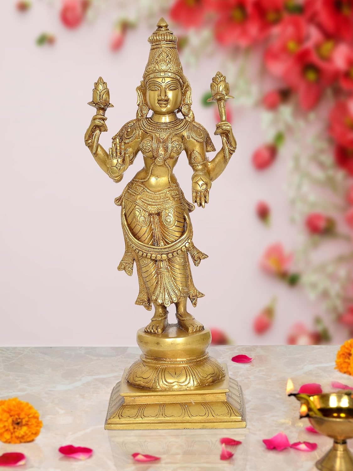 Brass standing Lakshmi goddess idol with four arms, ornate detailing, on pedestal.