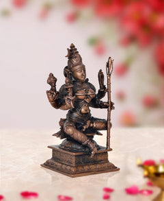 Rajarajeshvari statue angled view, seated four-armed goddess holding staffs, copper tone.