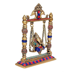 Angled view of brass Ganesha swing idol with colorful ornaments on gold frame