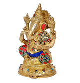 Brass Ganpati idol side view, red and blue clothing accents with gold ornaments, seated.