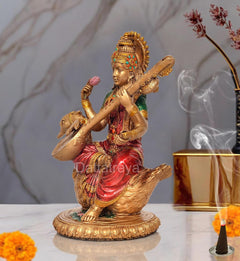 Side view of Saraswati idol resin statue on swan, veena held up; red and green attire
