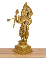 Side view of gold Krishna sculpture playing flute, intricate crown and flowing drapes