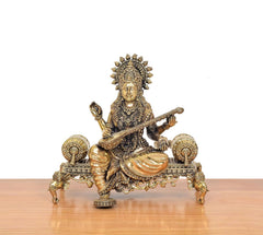 Saraswati brass idol seated on decorative throne, four ornate legs, veena across lap