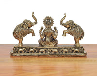 Side view of Lakshmi statue with elephants; ornate brass base and detailed engravings.