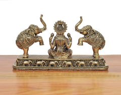 Side view of Lakshmi statue with elephants; ornate brass base and detailed engravings.
