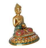 Brass Buddha statue angled view, seated posture with teal, red, and gold decor
