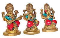 Three brass idols facing forward: Lakshmi, Saraswati, and Ganesha with teal-red accents