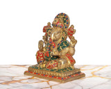 Seated Ganesha brass idol viewed from the side, multicolor accents on crown and garments