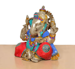 Brass Ganpati Bappa murti side view with red, blue and teal fabric panels and ornaments