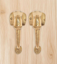 Brass Ganesha face door handle pair on light wood, two mounted levers