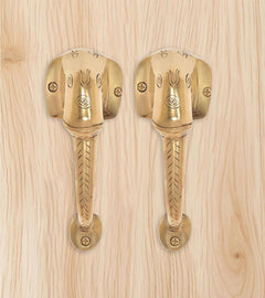 Brass Ganesha face door handle pair on light wood, two mounted levers