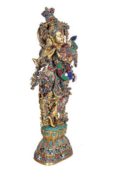 Side view of brass Krishna statue with flute, jeweled crown and multicolor garments