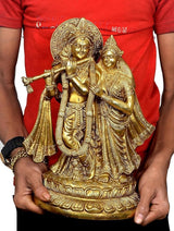 Brass Radha Krishna idol held by person, front view with crowns, flute, and robes