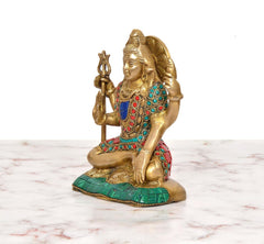 Side view of Lord Shiva brass statue seated with trident, jeweled multicolor attire