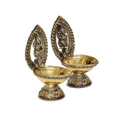 Two brass diya oil lamps with Lakshmi and Ganesha idols, angled view