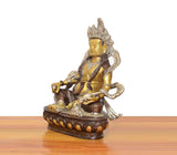 Brass Kuber Bhagwan murti, side view of seated deity with raised arms and ornaments