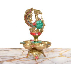 Side view of brass five-diya oil lamp stand, peacock on top with jeweled details