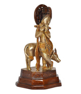 Brass Krishna statue riding cow, flute raised, sculpted details on circular backdrop