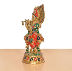 Side view of Krishna brass idol with multicolor halo and patterned red-green attire