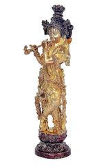 Side view brass Krishna playing flute figurine, ornate legs, standing on dark pedestal