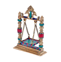 Gold brass Krishna jhula idol, side view with chain swing and turquoise/red tiled base