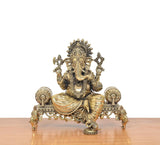Brass Ganesha idol seated on ornate singhasan with decorative four-armed hands