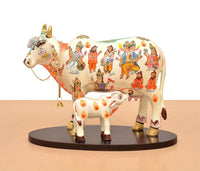 Two-piece resin cow and calf statue on a round base, white with colorful character artwork