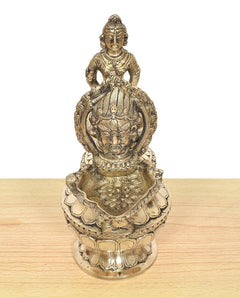 Brass oil lamp figure detail with seated deity and ornate face relief on base
