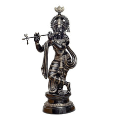 Brass Krishna statue with flute, standing on dark pedestal