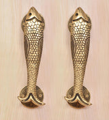 Two fish-shaped brass door handles with scale texture and curved tail ends.