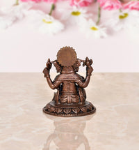 Copper Ganesha idol rear view with large crown and four arms, seated on lotus base