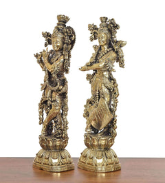 Brass Radha Krishna idol pair, angled view with raised hands and flared garments