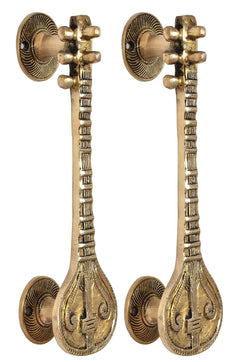Matching golden brass door handles with sitar motif, rosettes, and carved teardrop bases.